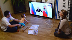 Молодая семья смотрит телевизионную трансляцию выступления президента РФ Владимира Путина Молодая семья смотрит телевизионную трансляцию выступления президента РФ Владимира Путина
