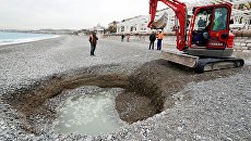 Экскаватор рядом с пятиметровым кратером, который сформировался на пляже Лидо в Ницце, Франция. 1 февраля 201 Экскаватор рядом с пятиметровым кратером, который сформировался на пляже Лидо в Ницце, Франция. 1 февраля 201