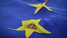 Дети выглядывают из прорезей во флаге ЕС во время акции протеста в Бухаресте, Румыния Дети выглядывают из прорезей во флаге ЕС во время акции протеста в Бухаресте, Румыния